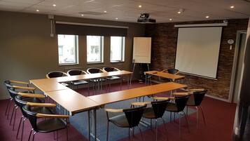 A conference room with a long table, chairs, a whiteboard, and a projector screen.