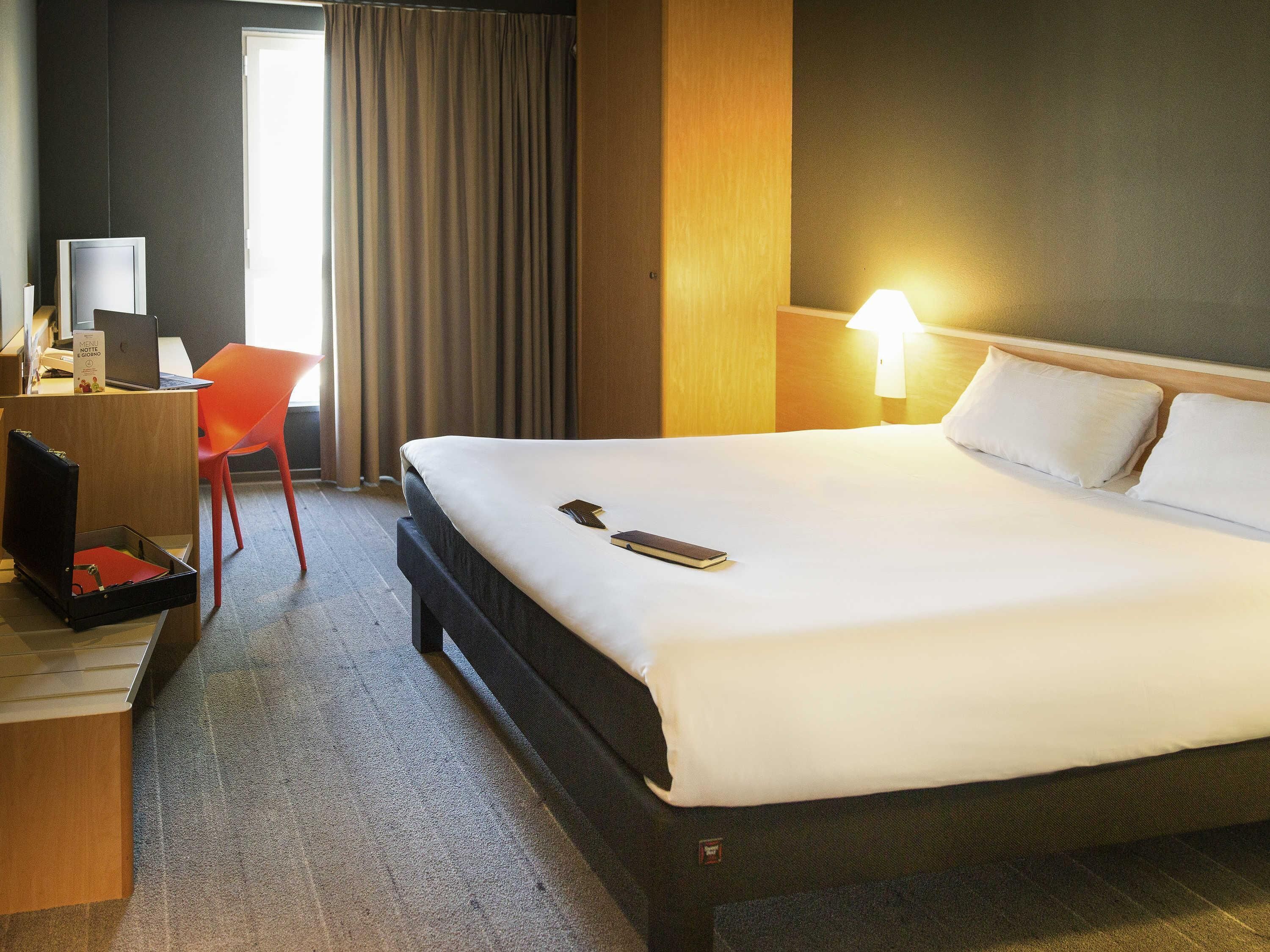 Une chambre d’hôtel avec un lit, un bureau avec un ordinateur portable, une chaise et une lampe de chevet.