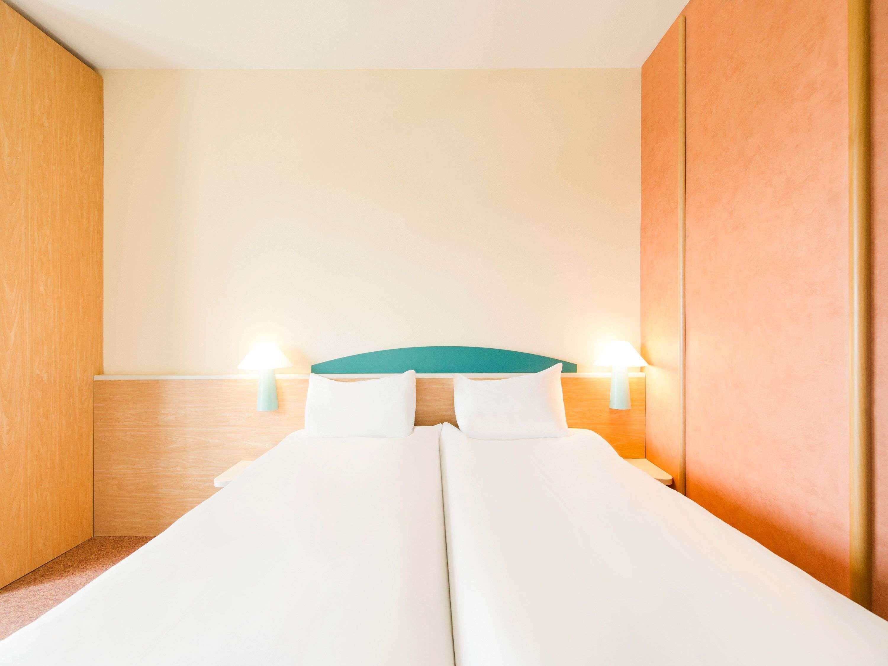 A hotel room with a double bed, two bedside lamps, and a wooden headboard.