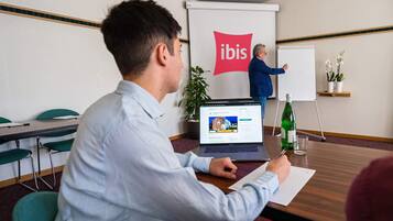 A conference room with a laptop, a whiteboard, and a presentation screen with the 'ibis' logo.