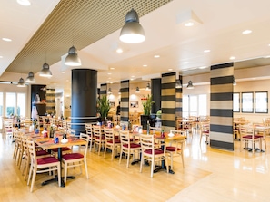 A spacious dining area with multiple tables and chairs, large pillars, and pendant lighting.
