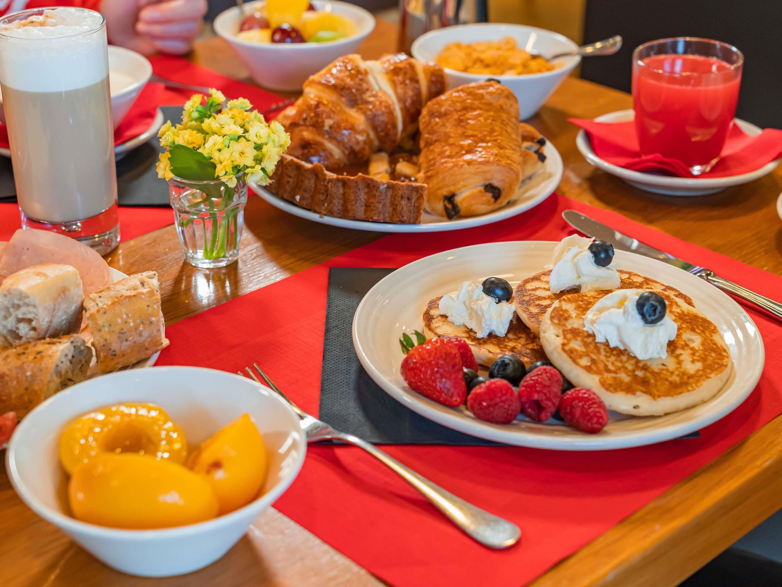 Un desayuno con tortitas, fruta y bollería sobre una mesa.