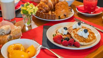 Un desayuno con tortitas, fruta y bollería sobre una mesa.