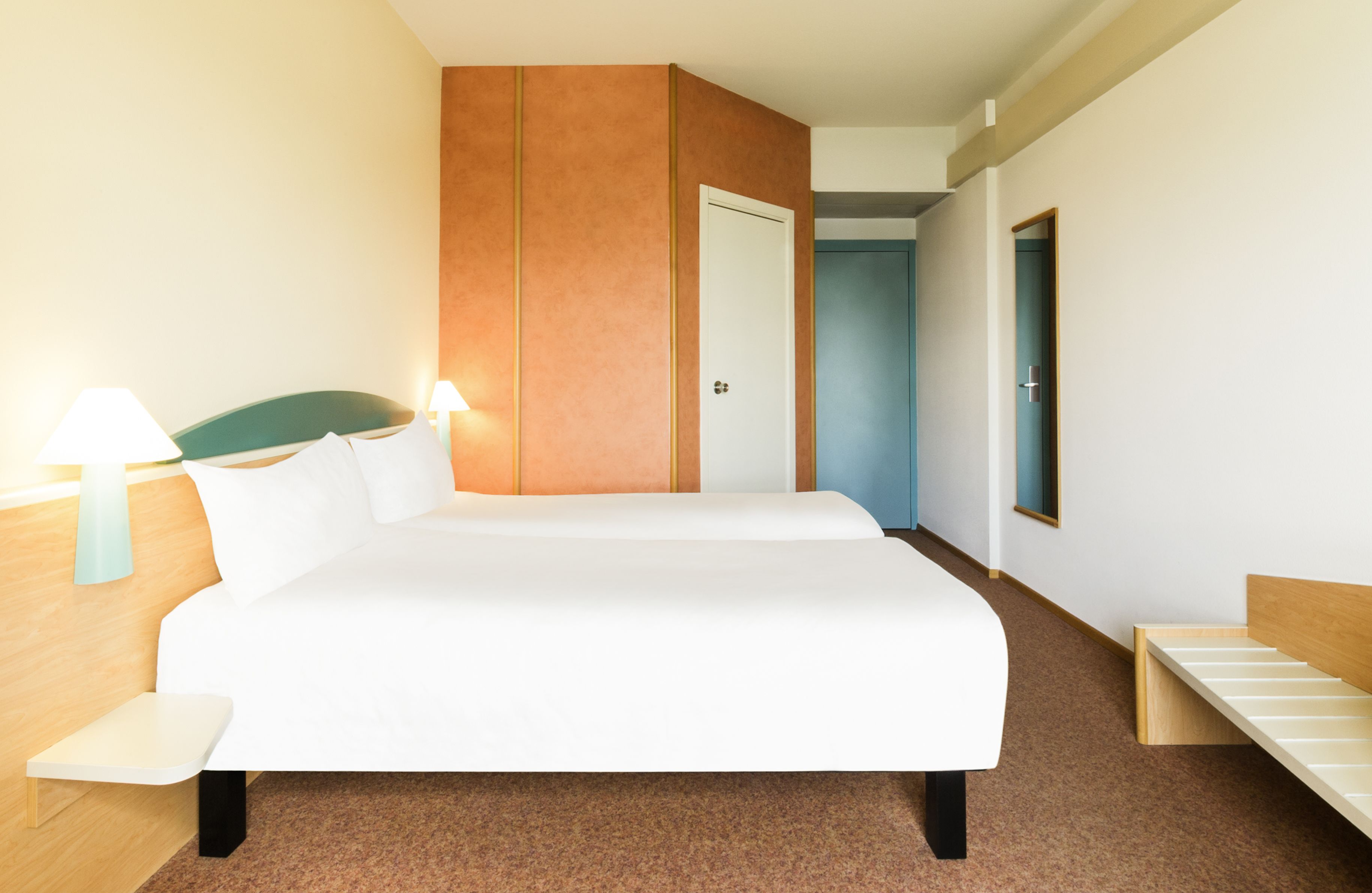 A hotel room with a large bed, bedside tables, a wardrobe, and a door leading to another room.