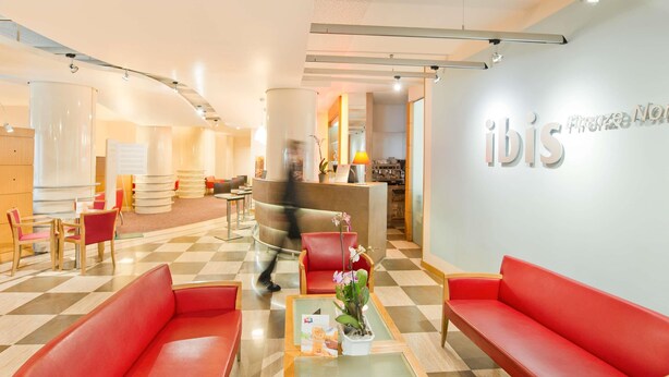 A hotel lobby with red seating, a reception desk, and a check-in counter. - ibis Firenze Nord Aeroporto (Sesto Fiorentino)