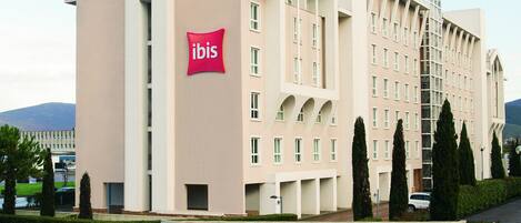 Een modern hotel met een opvallend 'ibis' logo, met een symmetrische gevel, meerdere balkons en een aangelegde binnentuin.