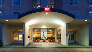 A hotel entrance with a red logo, a covered walkway, and red chairs. - ibis Firenze Nord Aeroporto (Sesto Fiorentino)