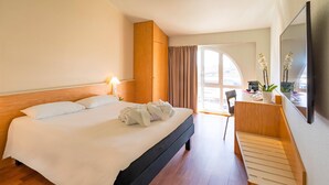 A hotel room with a bed, a desk, a chair, a mirror, and a view of the outdoors. - ibis Firenze Nord Aeroporto (Sesto Fiorentino)