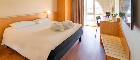 A hotel room with a bed, a desk, a chair, a mirror, and a view of the outdoors.