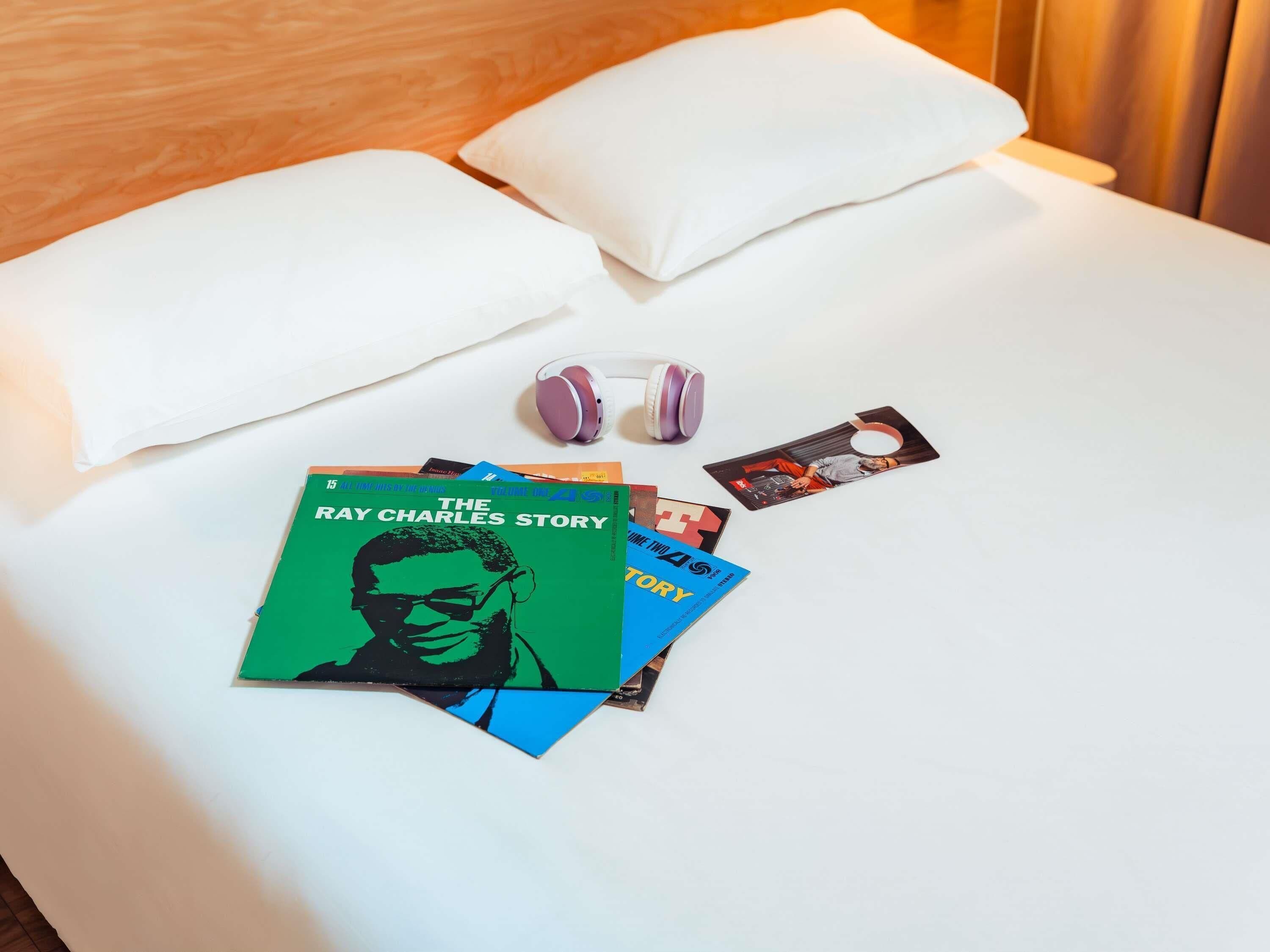 A neatly made bed with white sheets, a pillow, a pair of headphones, and a few books.