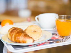 Una bandeja con cruasanes, una rosquilla, una taza de café y un vaso de jugo de naranja.
