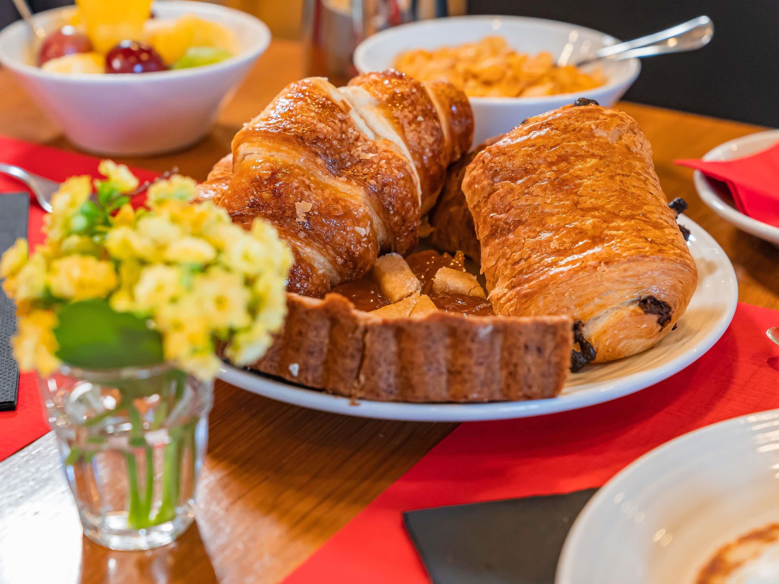 A dining table with a plate of croissants and a bowl of fruit.