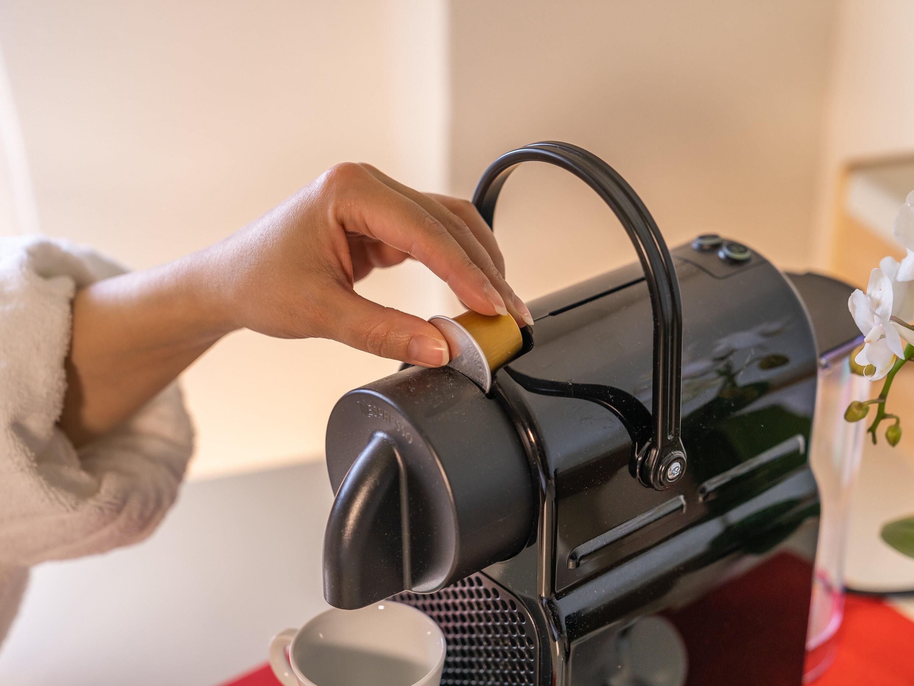 A hand operating a coffee machine with a cup placed underneath.