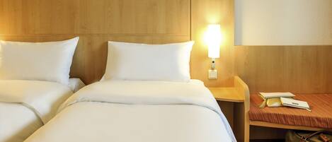 A hotel room with two beds, a nightstand with a lamp, and a suitcase.