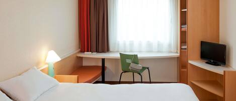 A hotel room with a bed, a desk, a chair, a television, and a window with curtains.