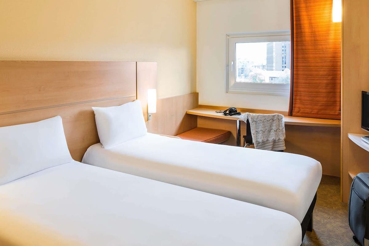 Habitación de hotel con dos camas, un escritorio, una silla, un televisor y una ventana con persianas.