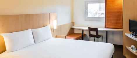 A hotel room with a large bed, a desk with a chair, a television, and a window with blinds.