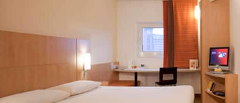 A hotel room with a bed, a desk, a chair, a television, and a window with curtains.