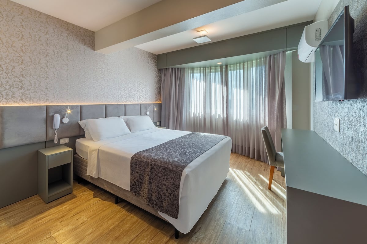 A modern hotel room with a large bed, bedside table, and a desk area.