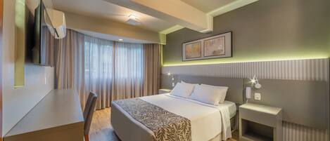 Habitación de hotel moderna con una cama grande, mesita de noche y un escritorio con una silla.