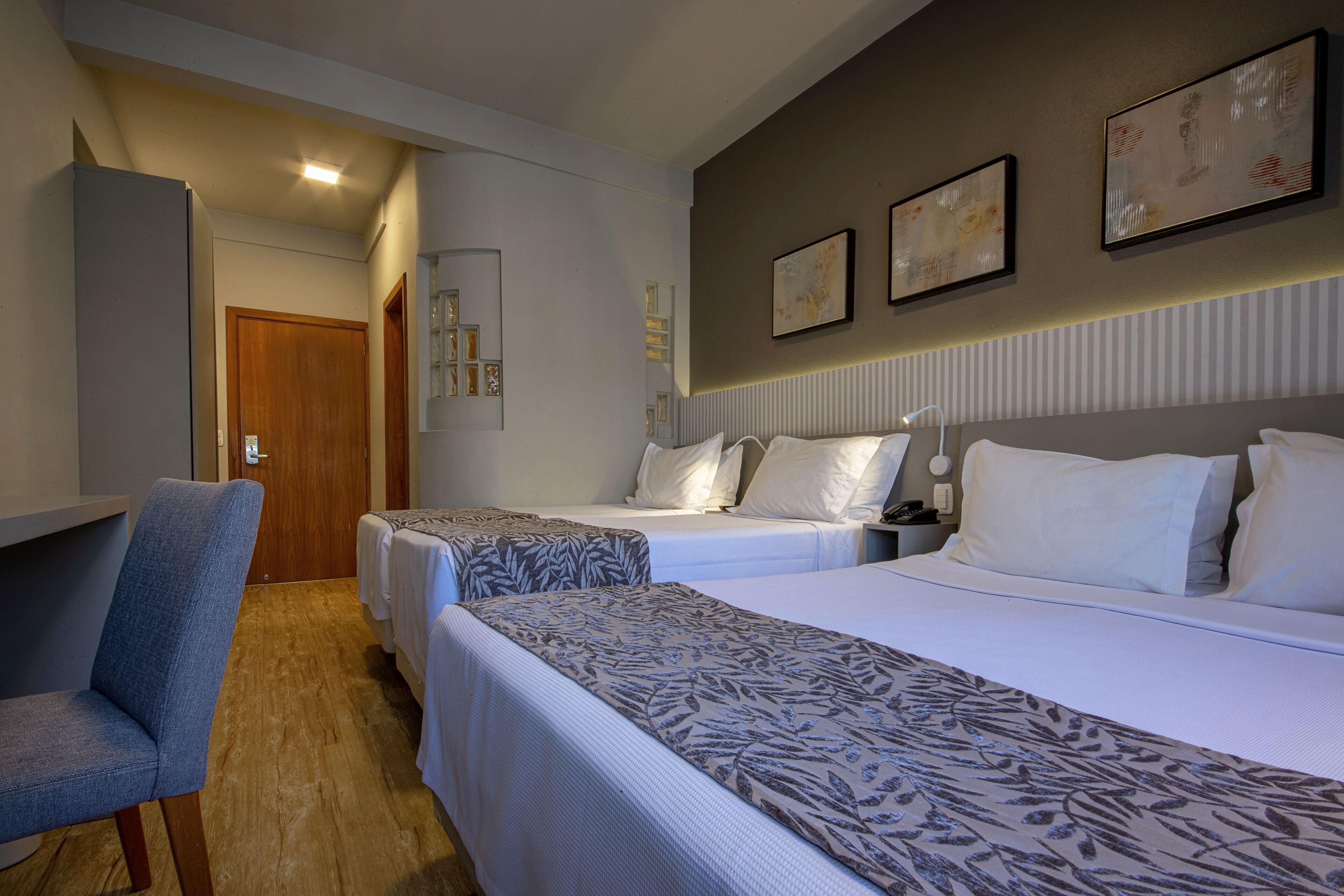 Une chambre d’hôtel avec deux lits, un bureau et une chaise. Des lampes murales et des œuvres d’art encadrées sont disposées au-dessus des lits.