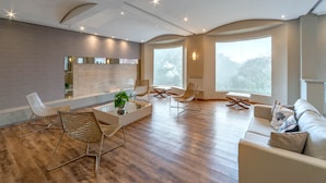 A spacious living room with a modern design, featuring a sofa, chairs, a coffee table, and large windows providing natural light. - Hotel Laghetto Siena (Gramado)