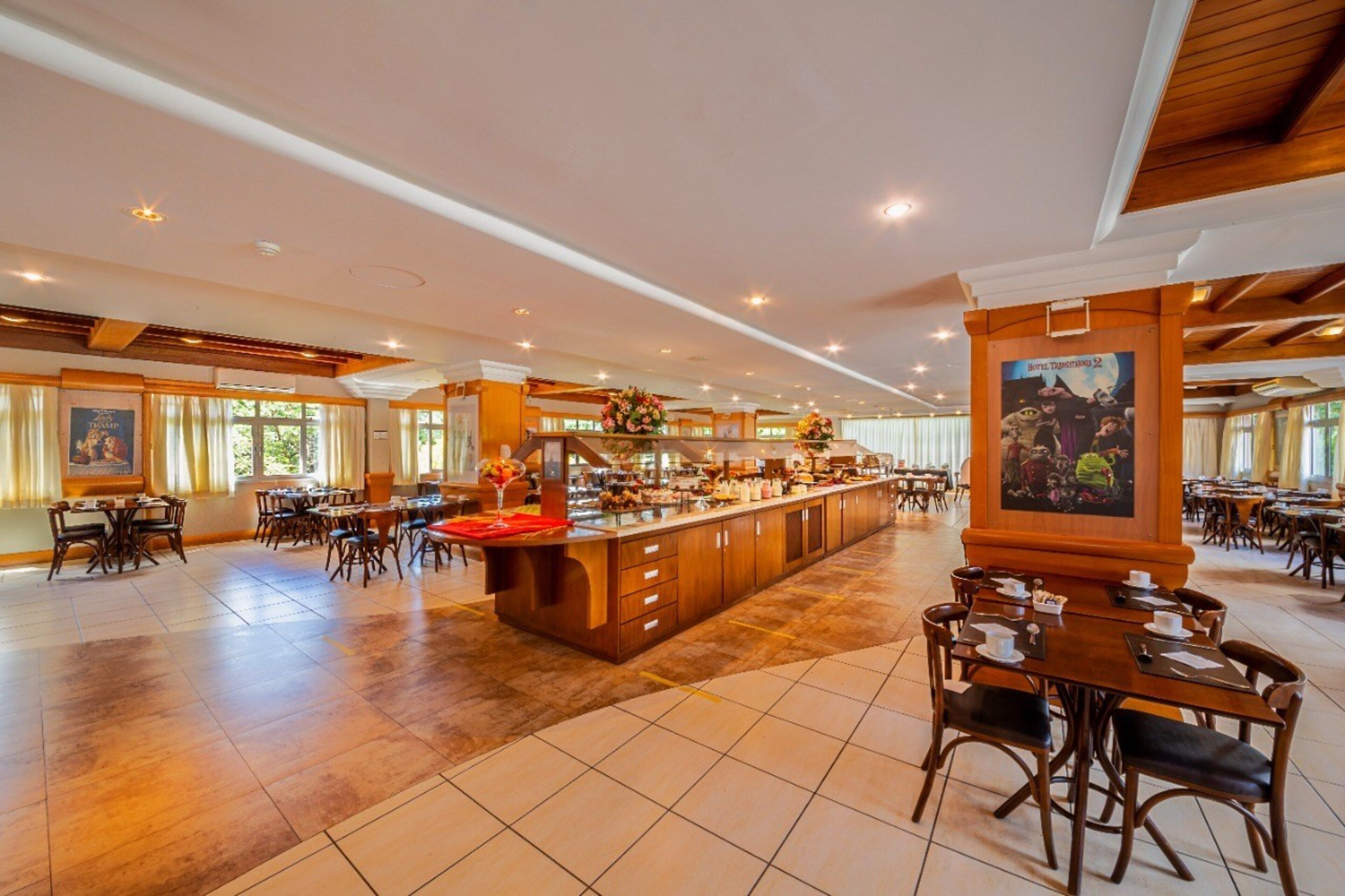 A spacious hotel lobby with a central bar area, multiple dining tables, and a large painting on the wall.