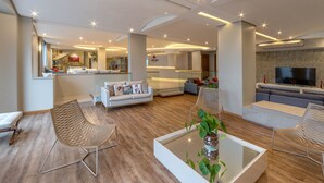 A spacious living area with a modern design, featuring a sofa, chairs, a coffee table, and a TV. - Hotel Laghetto Siena (Gramado)