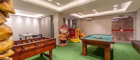 A children's play area with a foosball table, a pool table, and a play structure.