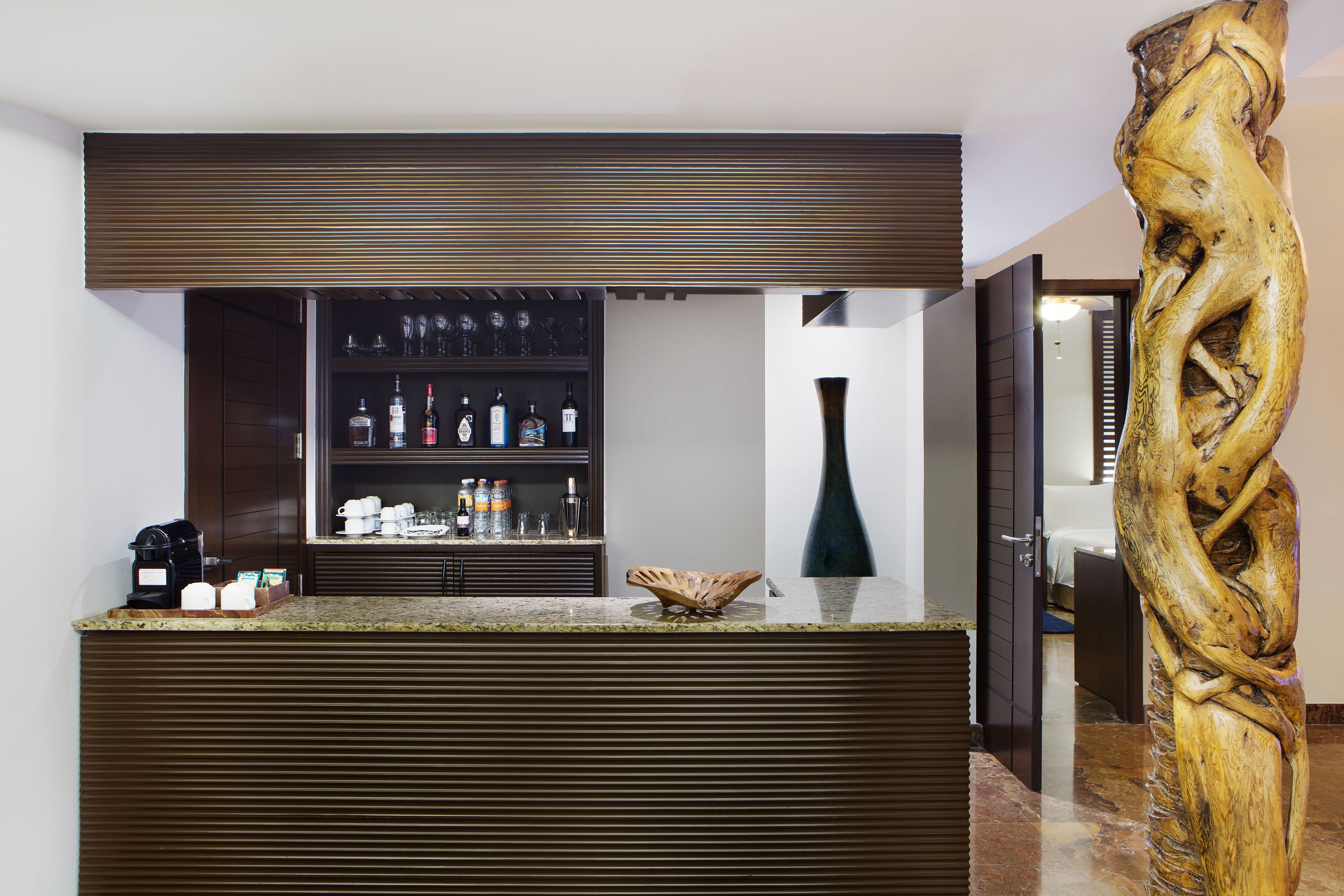 Un espace bar doté d’un comptoir en bois, d’étagères remplies de bouteilles et d’un vase décoratif.