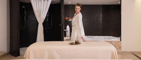 A spa room with a massage table, a bathtub, and a shower area.