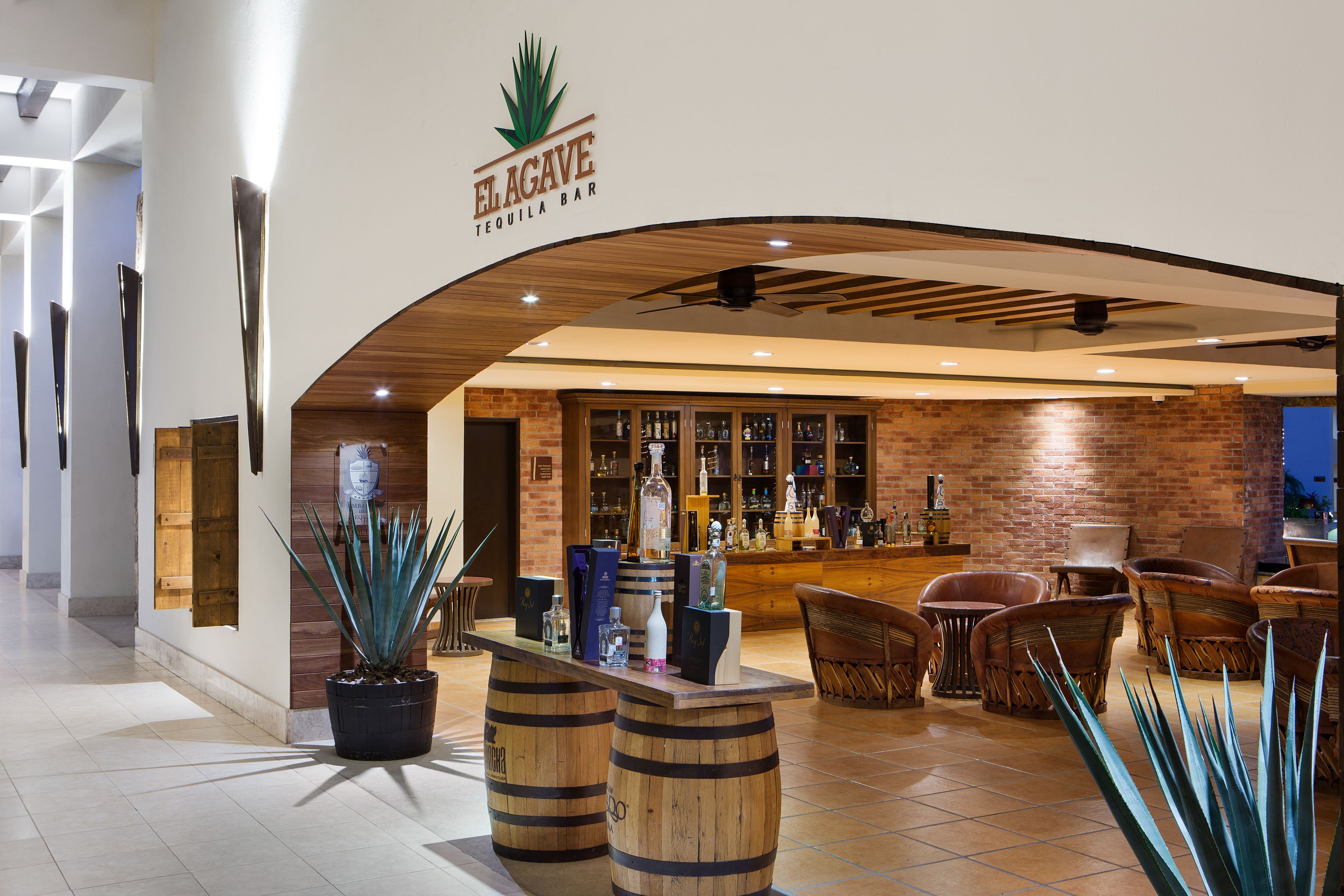 Zona de bar con barra de madera, asientos y exhibición de licores a la vista.