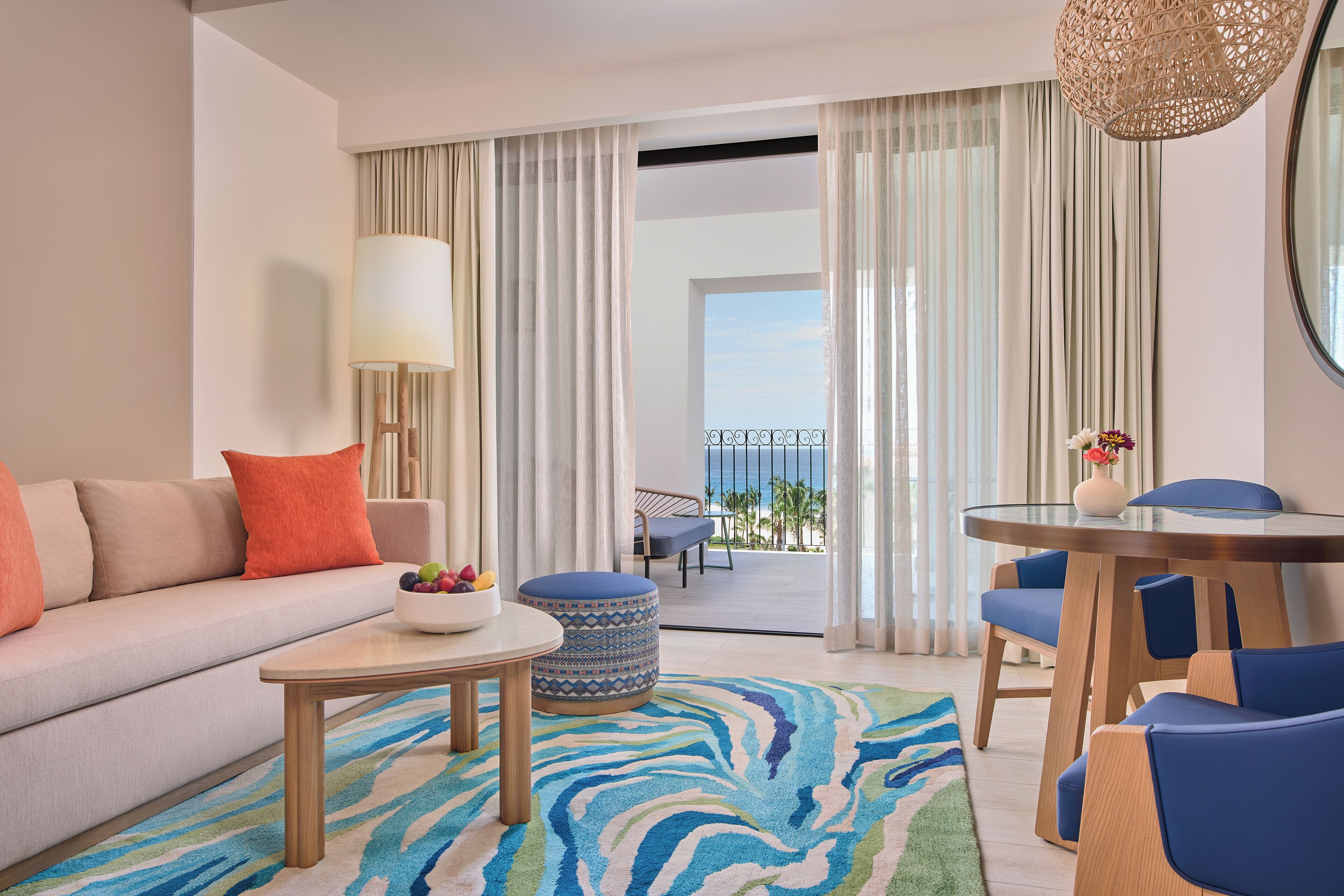 Ett modernt hotellrum med en soffa, ett matbord och stolar. Genom de stora fönstren har man utsikt över havet.