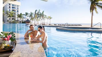 A couple relaxing in a pool with a view of the beach and palm trees.