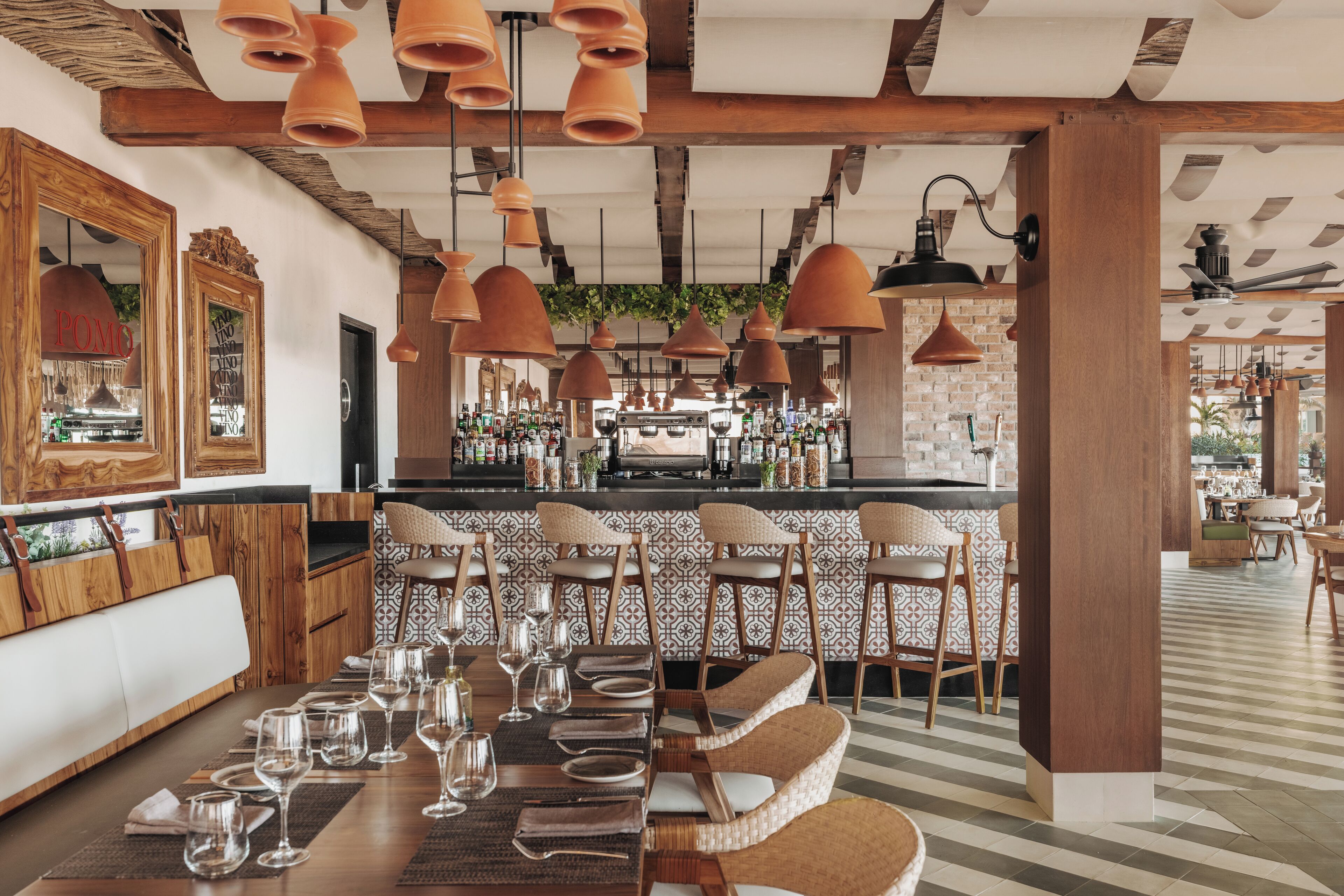 A restaurant with a bar area, wooden furniture, and terracotta pendant lighting.