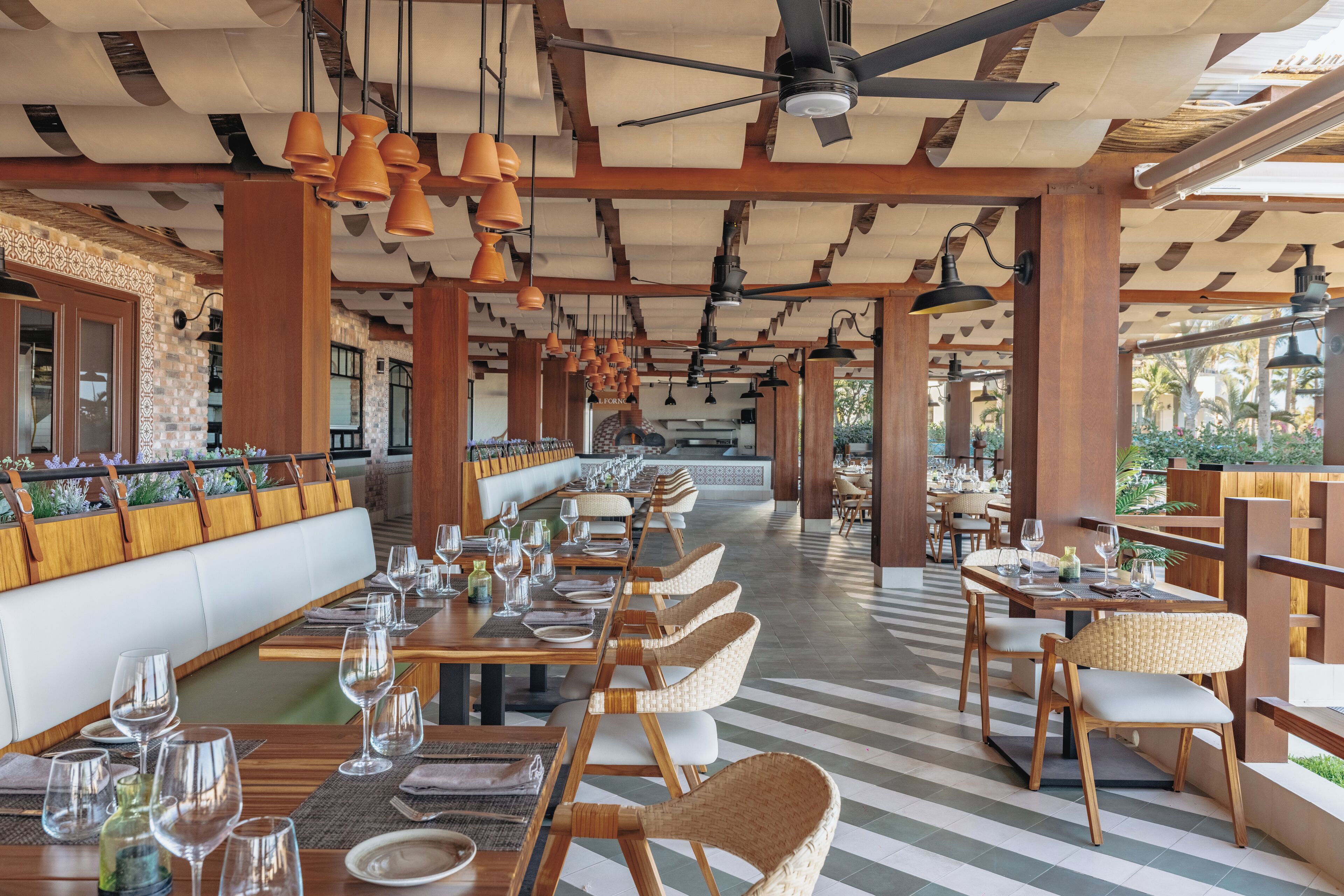 Un restaurant spacieux avec de hauts plafonds, des poutres apparentes et un mélange de sièges en bois et de sièges rembourrés. Les tables sont dressées avec des verres à vin et des assiettes, et le sol présente un motif de carreaux à rayures.