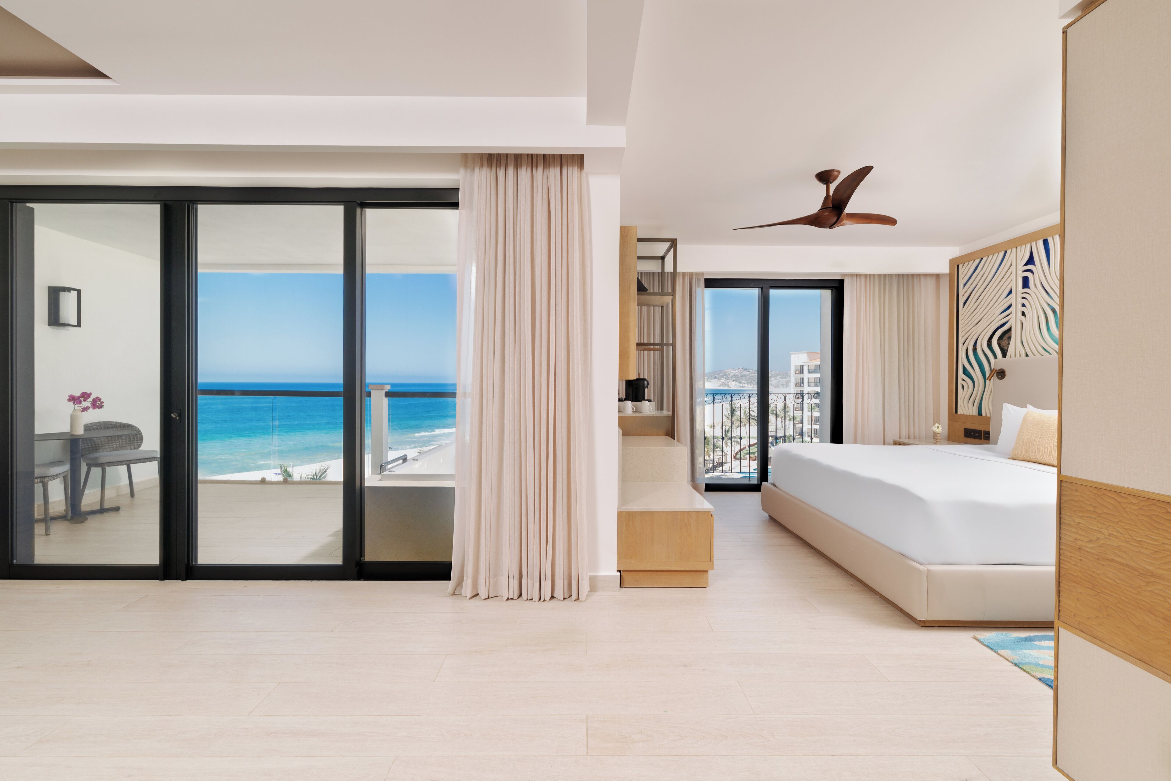 A modern hotel room with a large bed, a ceiling fan, and a view of the ocean.