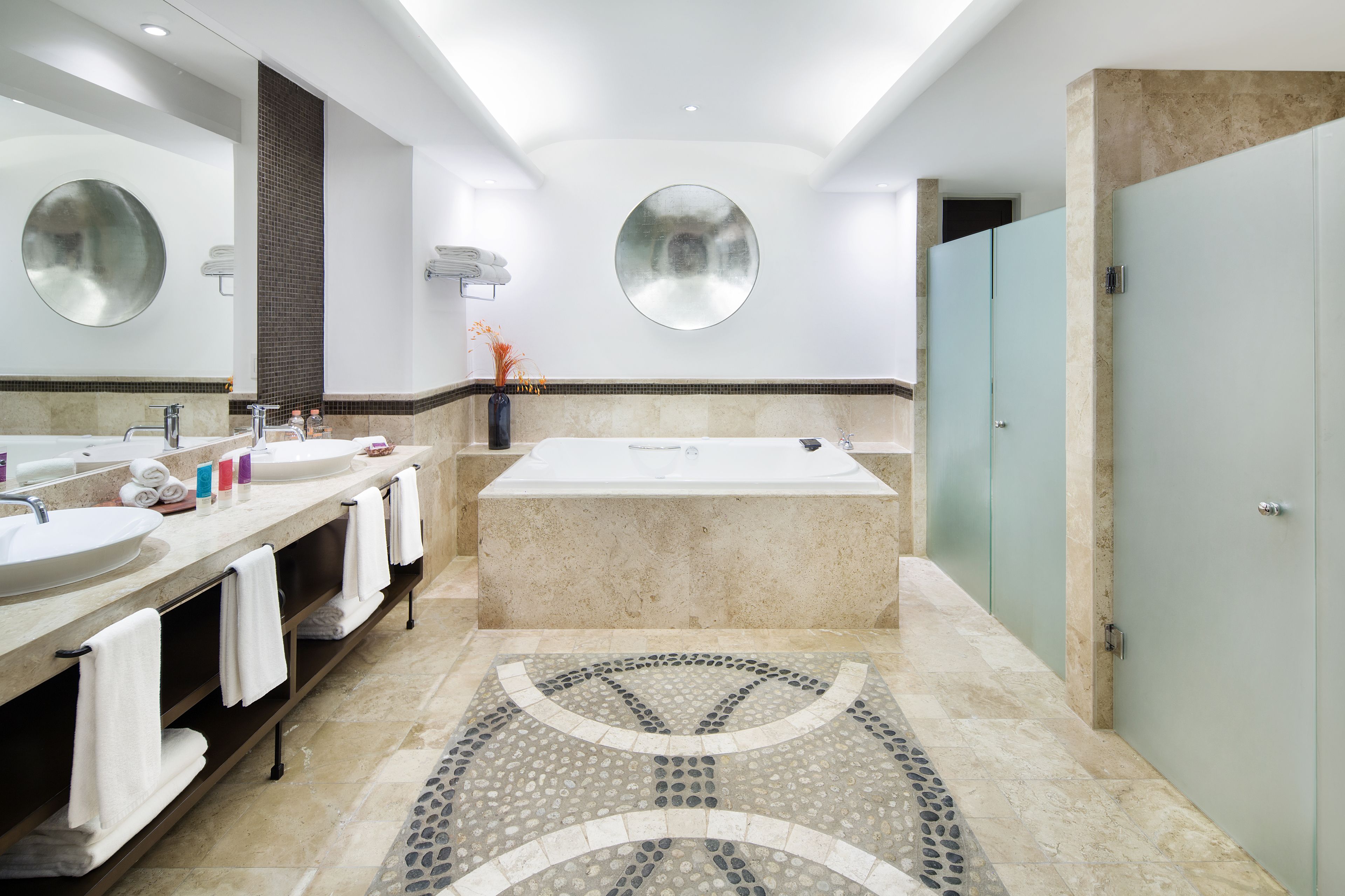 Une salle de bain moderne avec deux lavabos, une grande baignoire et un miroir rond.