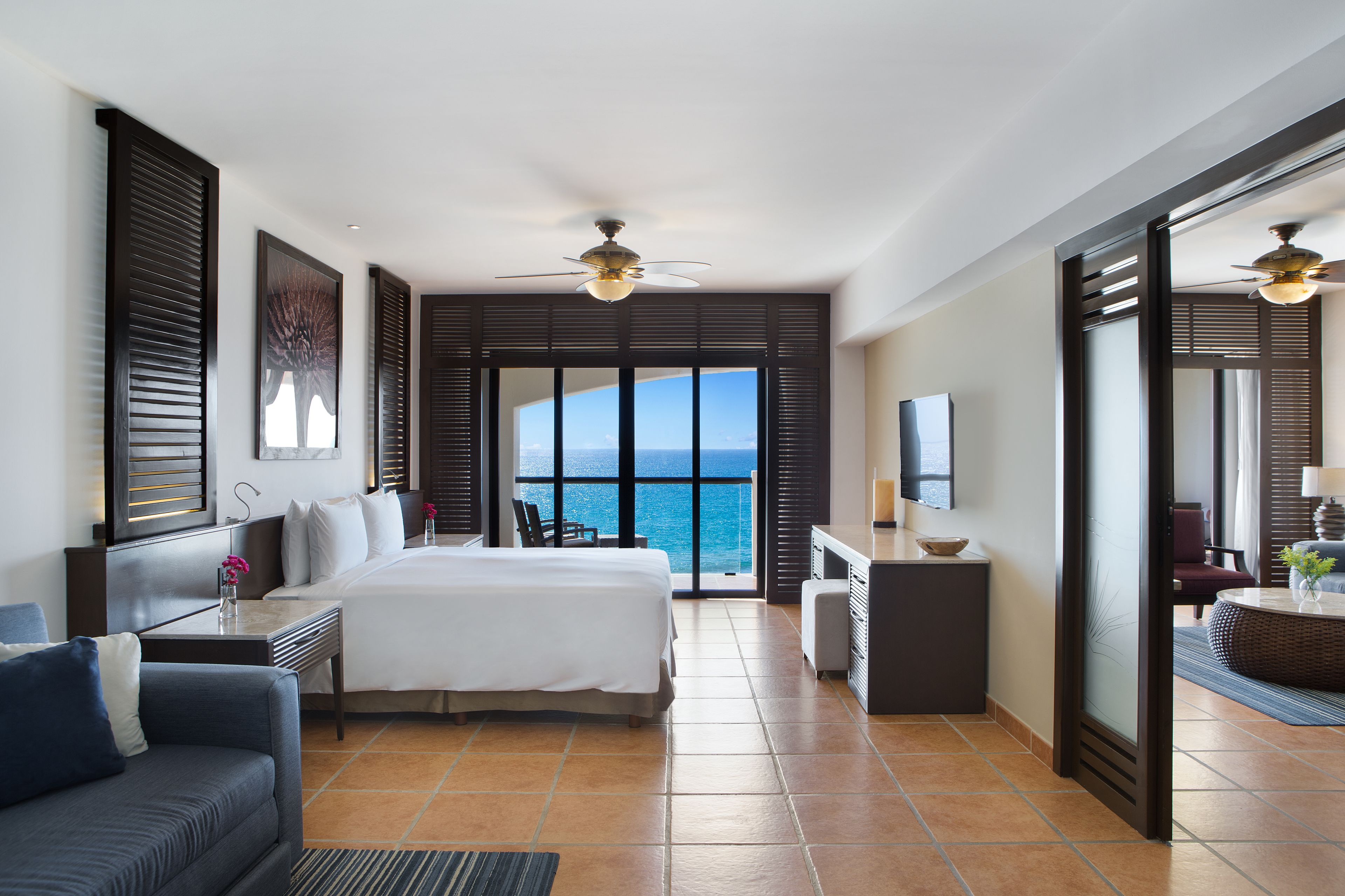 A hotel room with a bed, a desk, a chair, and a view of the ocean.