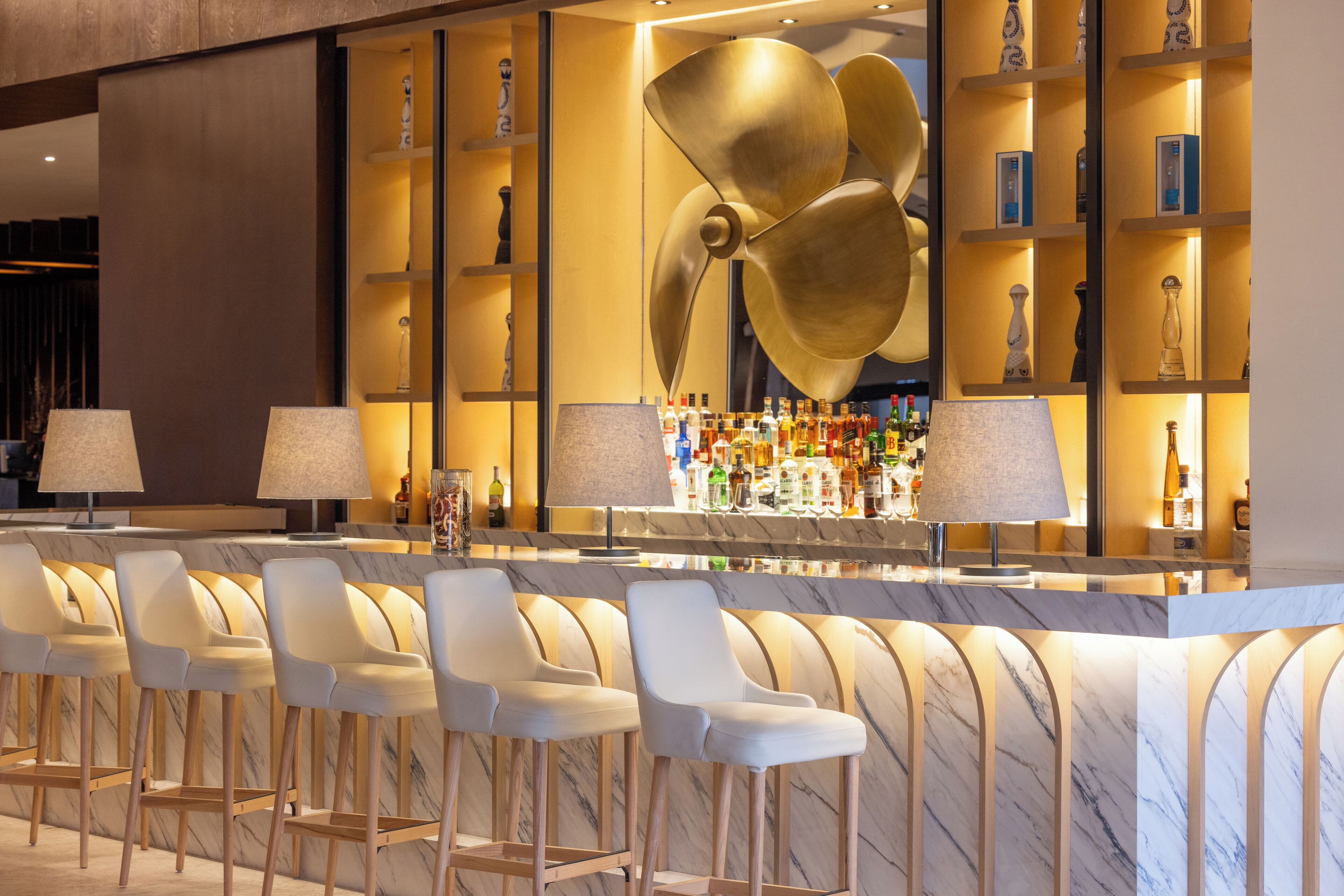 A bar area with marble countertops, bar stools, and a large decorative fan.