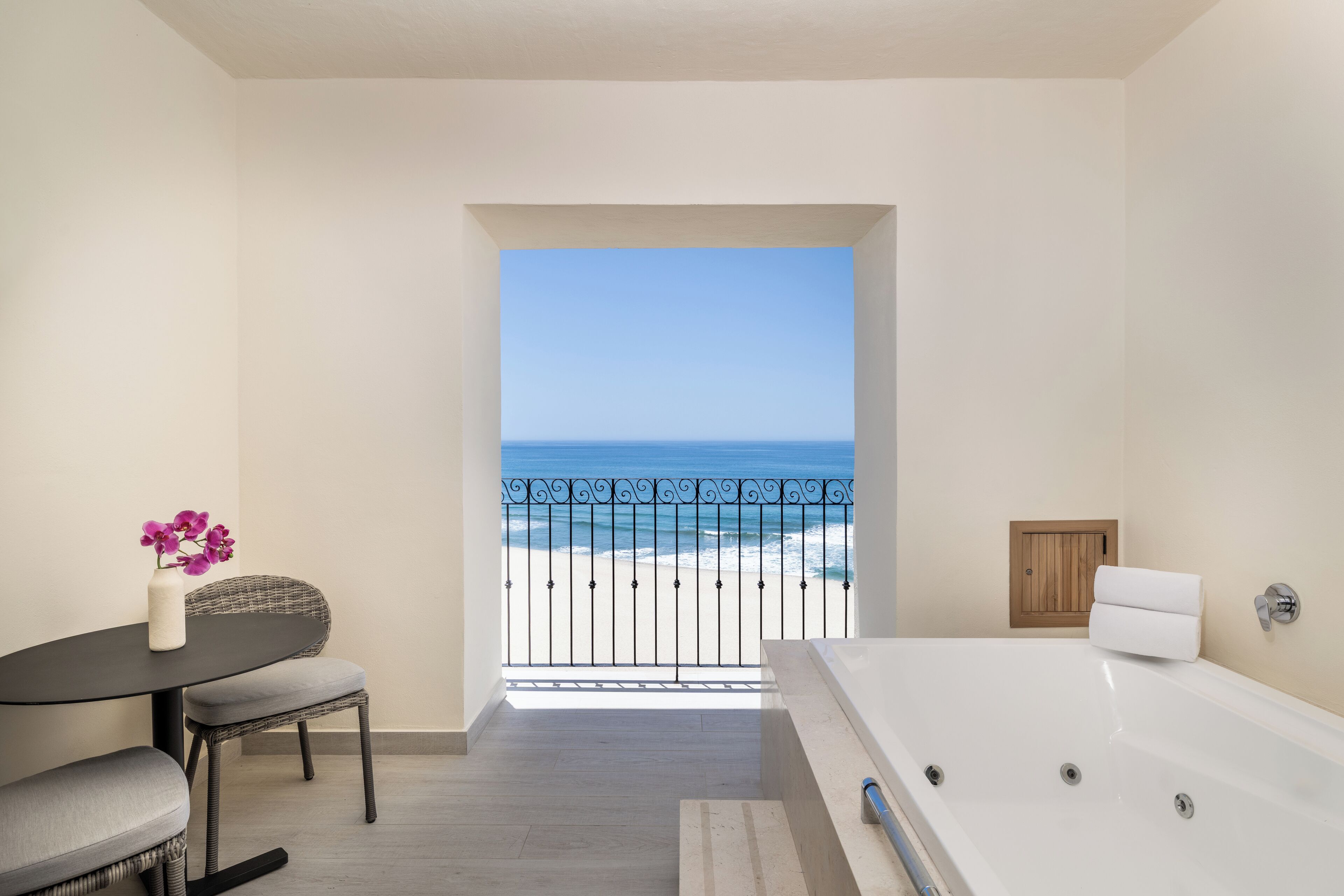 Un baño con bañera, una mesita con un florero y vistas a la playa desde el balcón.