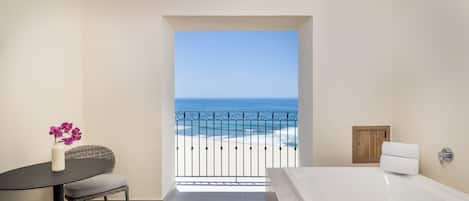 Un baño con bañera, una mesita con un florero y vistas a la playa desde el balcón.