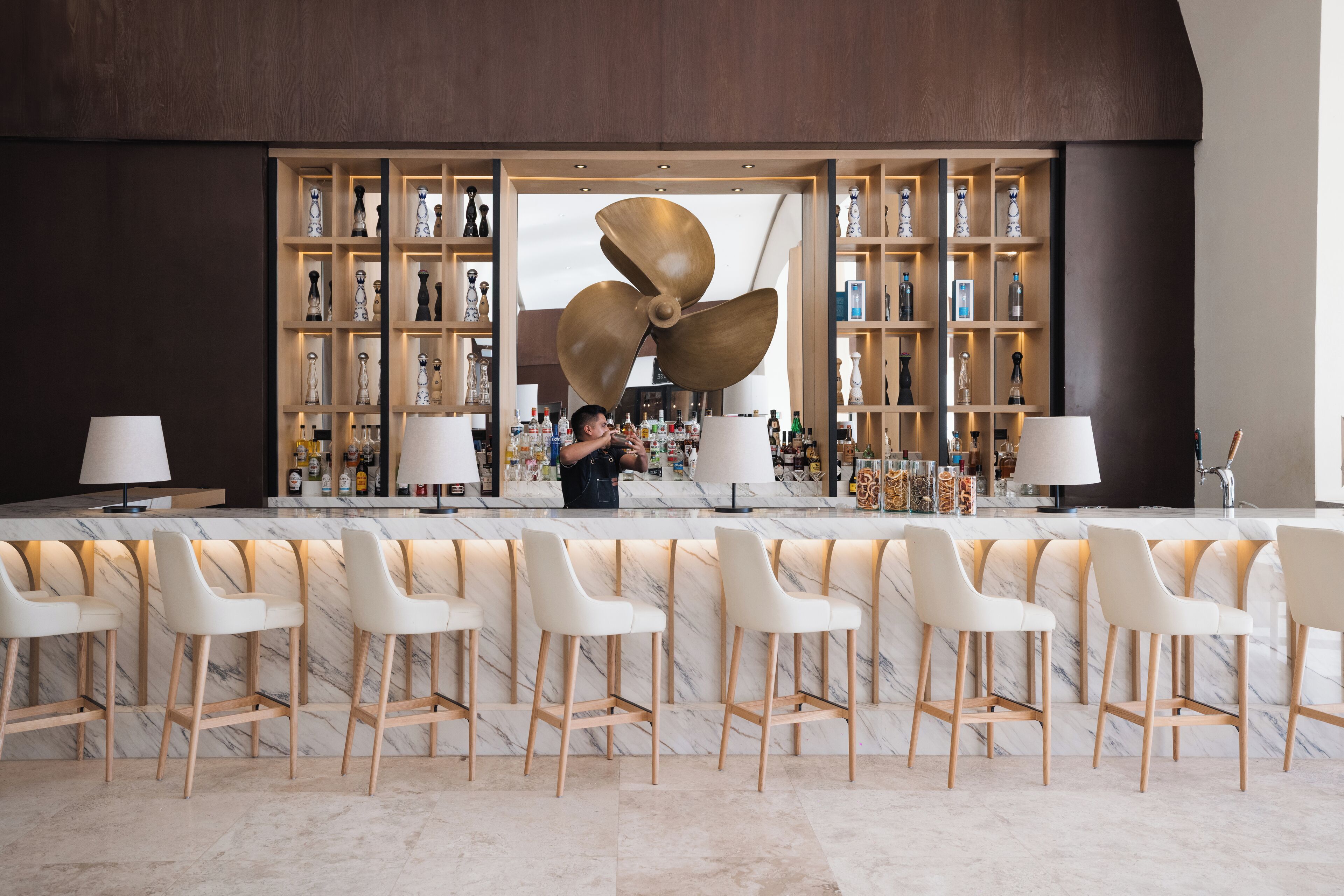 A bar area with a large fan, marble bar counter, and multiple white bar stools.