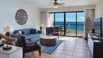 Una habitación de hotel moderna con balcón, un sofá, una silla, una mesa de centro y un televisor.
