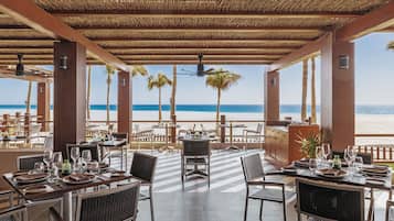 Un restaurante frente al mar con mesas dispuestas para comer, techo de paja y vista al océano.