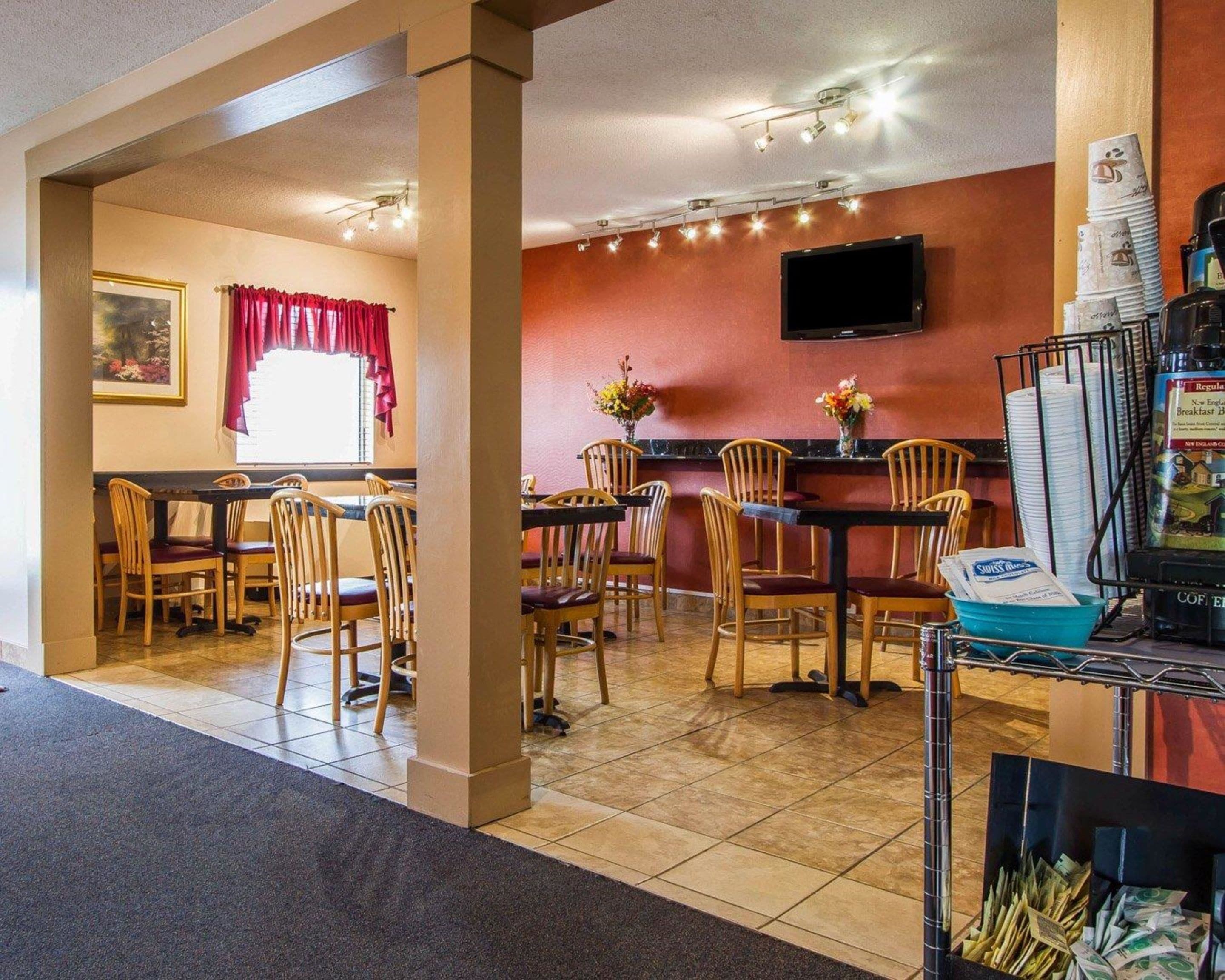 Un restaurant avec des chaises et des tables en bois, un téléviseur fixé au mur et une machine à café.