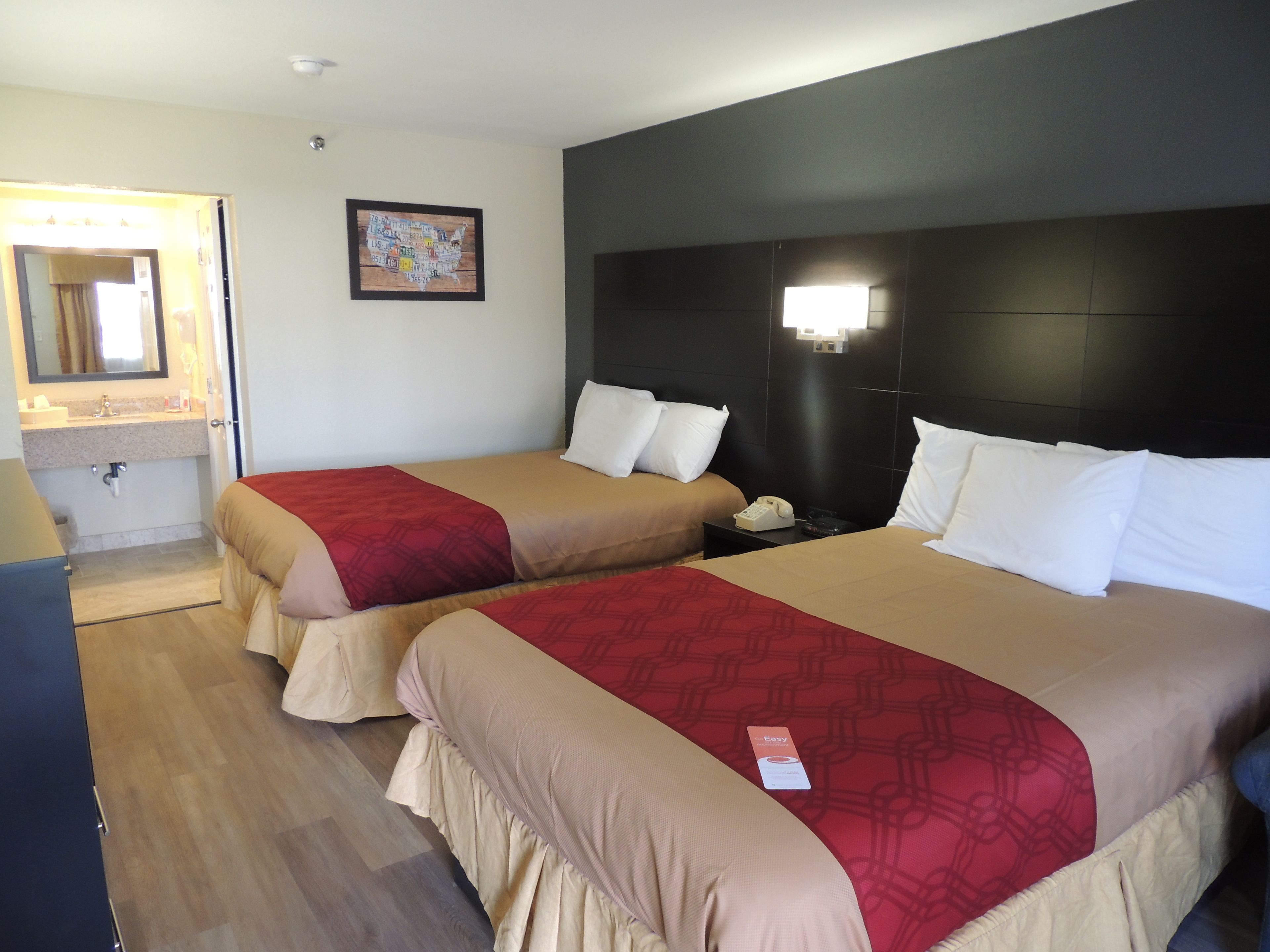 Habitación de hotel con dos camas, una mesita de noche con teléfono, un espejo y una lámpara de pared.