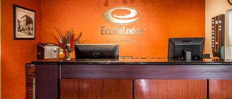 A reception desk at Econolodge with a wooden finish, a framed picture on the wall, and a clock.