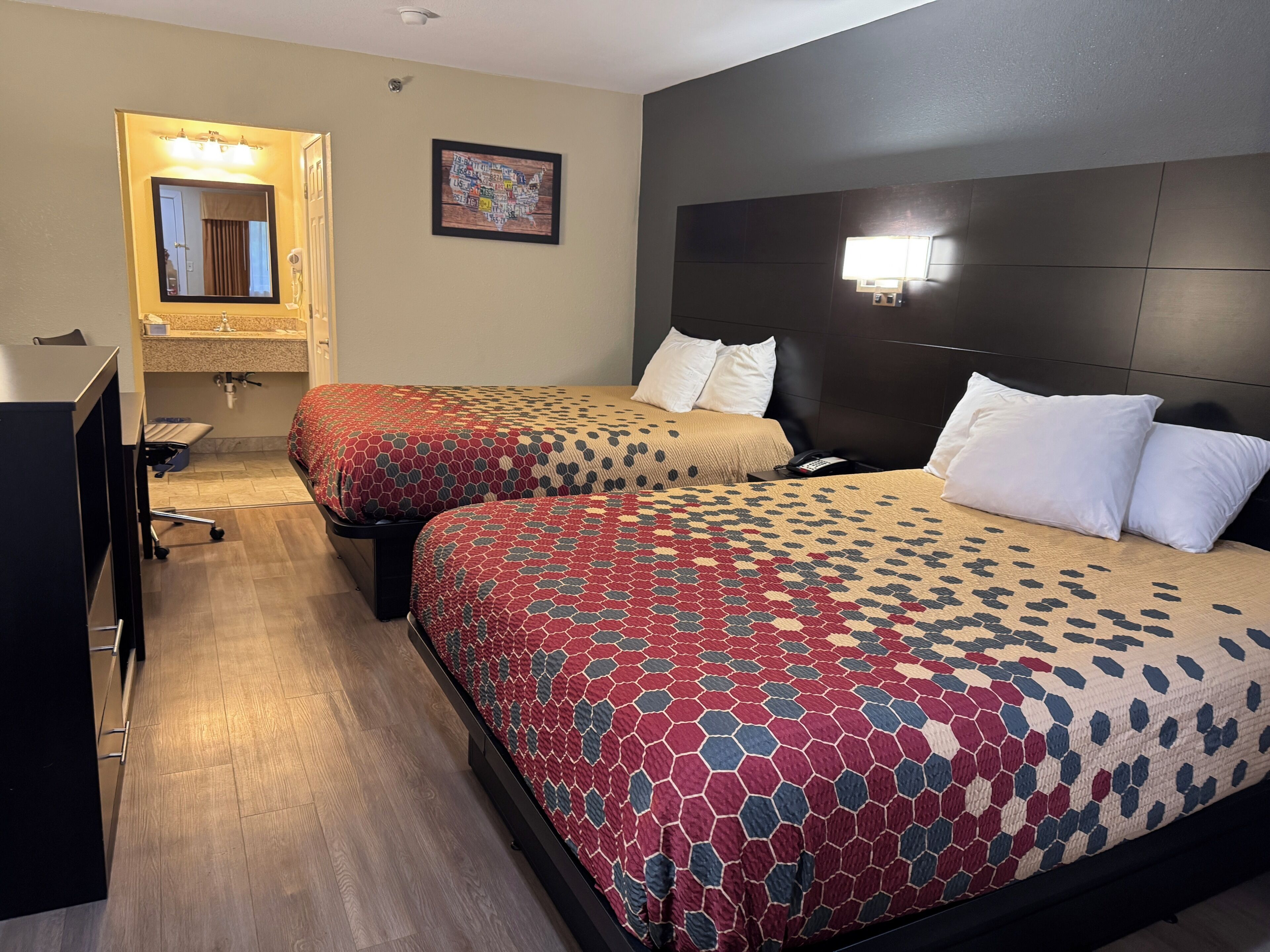 Habitació d'hotel amb dos llits, un escriptori, un mirall i una làmpada de paret.