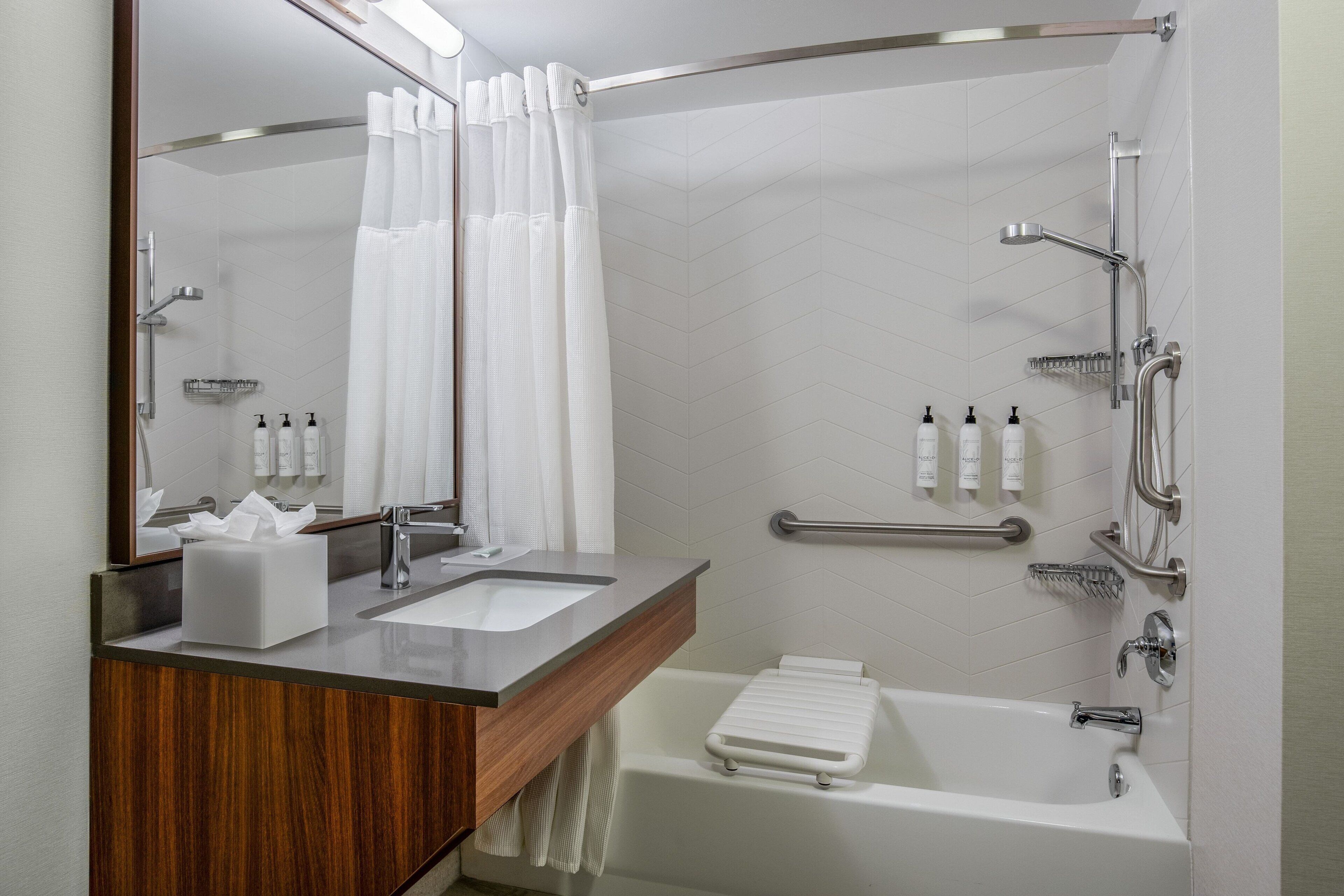 A modern bathroom with a wooden vanity, a large mirror, a shower with a handheld showerhead, and a bathtub.